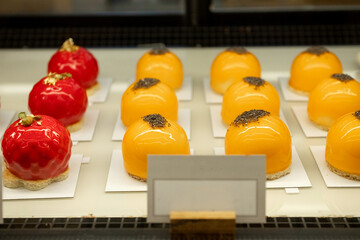 Orange and red dome-shaped pastries with glossy glaze on display.