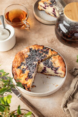 Blueberry cake on a plate sprinkled with powdered sugar on beige background with tea