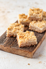 Lemon crumble bars on wooden cutting board on light textured background, oatmeal lemon bars
