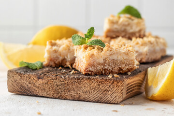 Lemon crumble bars on wooden cutting board on white tile background. Oatmeal lemon bars