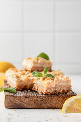 Lemon crumble bars on wooden cutting board on white tile background with text space. Oatmeal lemon bars