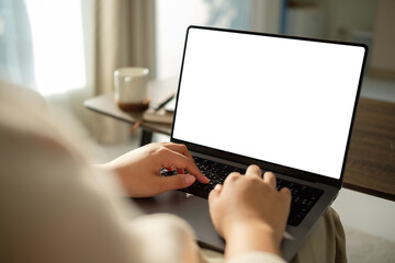 Close-up of hands typing on a laptop with a blank white screen. Workspace with coffee cup in a cozy...