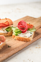 Delicious sandwiches with cream cheese, salami, cucumber, tomatoes on wooden board on light background. Homemade appetizer