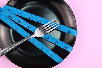 Plate with stainless steel fork and tape measure on isolated background. Healthy eating or dieting...
