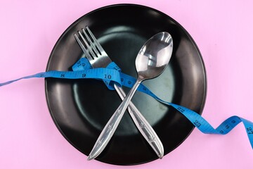 Healthy eating or dieting concept. fork and spoon wrapped in blue measuring tape on empty plate...