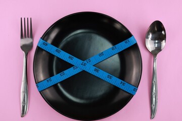 Black plate and cutlery in the form of a spoon with a fork on a pink isolated background with a...