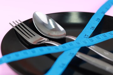 Healthy eating or dieting concept. fork and spoon wrapped in blue measuring tape on empty plate....