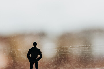 A man standing with his back facing us, gazing out of a window and lost in thought. A silhouette of...
