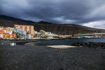 Houses and buildings in the town of Panta del Hidalgo on the Atlantic Ocean coast on the island of Tenerife with mountains in the background under a cloudy sky	
