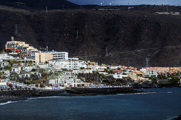 Houses and buildings in the town of Panta del Hidalgo with an inscription on concrete barriers on the shore of the Atlantic Ocean on the island of Tenerife with a mountain in the background	
