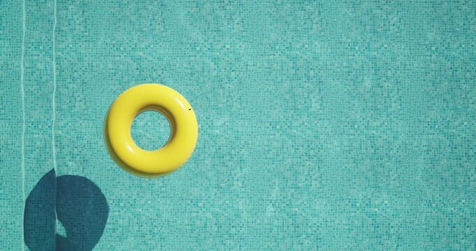 Top view of a bright yellow inflatable ring floating on clear turquoise water in a swimming pool. Sunlight casts a distinct shadow on the mosaic tiles. Minimal, peaceful summer vacation vibe