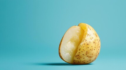 Close-up of a single potato on a blue background. the potato is cut in half, revealing the yellow flesh inside.