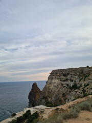 Coastal cliff overlooking the ocean under a cloudy sky. The rocky formation juts out into the...
