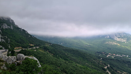 A panoramic view of a lush green valley surrounded by mountains under a cloudy sky. The landscape...
