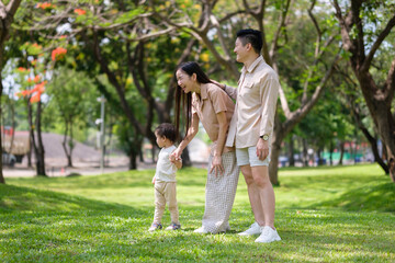 Happy Asian family spending quality time together in a green park. Parents and child enjoying...