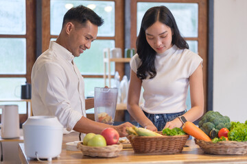 Happy couple preparing fresh fruit smoothies together in a cozy kitchen. Wellness and healthy lifestyle concept.
