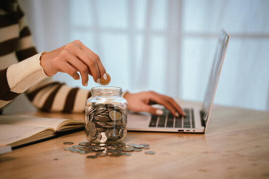 A young woman manages her finances at home using a laptop and coin jar, focusing on savings, budgeting, investment, and digital banking for future financial security.