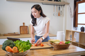 Happy female cooking a nutritious meal at home while following a recipe on digital tablet.