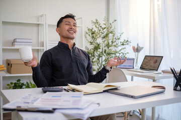 Fototapeta premium Relaxed businessman enjoying a coffee break while meditating at his modern office desk.