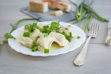 Hot dumplings in a plate with onions on a light wooden table