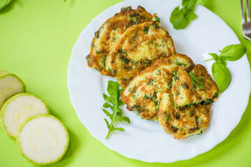 appetizing zucchini pancakes with green onions in a plate on a green background