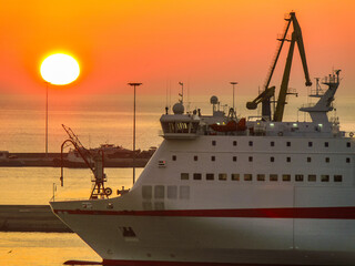 A majestic sunrise bathes the Heraklion Port in golden light as a passenger ferry stands still,...