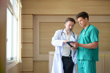 Senior male doctor explains test results to a young man doctor on digital tablet, teaching and...