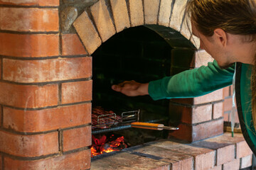 A man is cooking delicious meat in a traditional brick oven and checks temperature