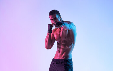 Male boxer in hand wraps practicing punches on purple neon background during intense workout...