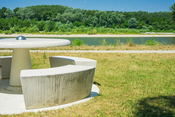 A stone picnic table with benches on a sunny day by a river, concept of outdoor furniture, park design, and travel destinations