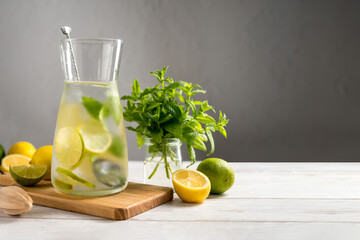 A glass jug with lemonade with lemons, limes and fresh mint, summer drink. Copy space