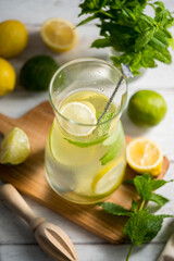 A glass jug with lemonade with lemons, limes and fresh mint, summer drink