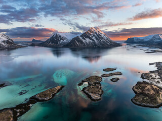 Snow-capped mountains reflected in calm sea at sunset