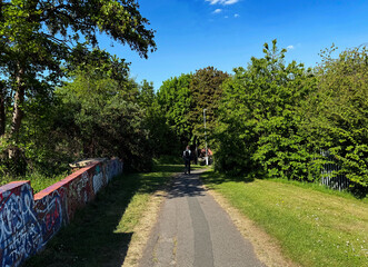 A paved path, surrounded by lush greenery and trees under a clear blue sky. Graffiti-covered walls add an urban touch to the otherwise natural setting in, Woodhouse, Leeds, UK