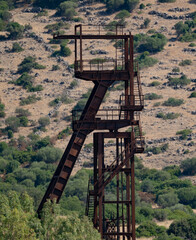 Rusty industrial tower stands isolated against a dry hillside covered with sparse vegetation