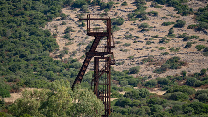 Rusty industrial tower stands isolated against a dry hillside covered with sparse vegetation