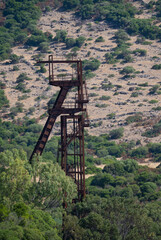 Rusty industrial tower stands isolated against a dry hillside covered with sparse vegetation