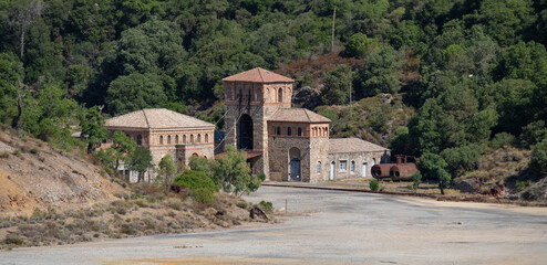 Rusty industrial tower stands isolated against a dry hillside covered with sparse vegetation