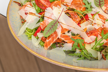 A vibrant fresh salad with slices of salmon, parmesan cheese, arugula, cherry tomatoes, and greens, beautifully garnished with a drizzle of balsamic glaze