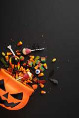 Brightly colored Halloween candies scattered from a pumpkin bucket with festive decorations, captured on a black vertical background, evoking a festive and spooky Halloween celebration © ActionGP