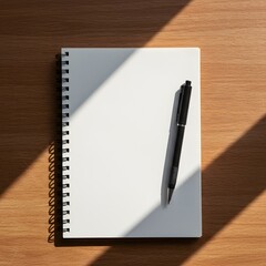 Overhead view of a blank notebook and pen resting on a wooden surface, bathed in sunlight.