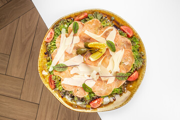 A beautifully plated salmon carpaccio with parmesan shavings, fresh greens, cherry tomatoes,...