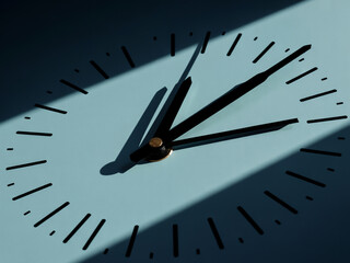 The hands of a clock cast shadows on a light blue surface