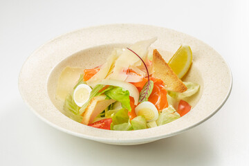 A fresh and colorful salad with smoked salmon, parmesan shavings, lettuce, cherry tomatoes, croutons, and quail eggs, garnished with a lemon wedge in a light ceramic bowl