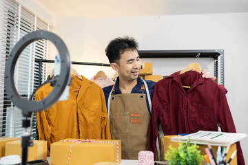 A man is selling clothes online, using his mobile phone. He is live selling with fun. He is smiling...