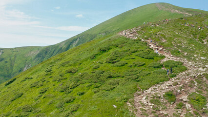 Aerial view of young tourists walking along a mountain trail to the top of the mountain.