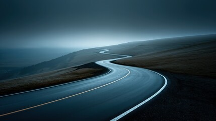 Serene winding road cutting through rolling hills under a mist - laden sky. Ideal for travel, adventure, or nature - themed projects. 