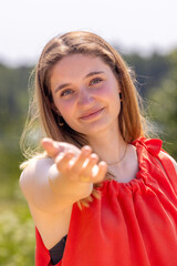 In a scenic outdoor setting, a woman in a vibrant red dress extends her hand, inviting genuine connection