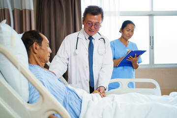 Doctor and nurse visit elderly male patient in recovery ward in hospital.