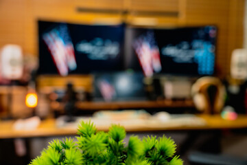 Modern home office desk setup with American Independence Day theme, including monitors displaying US flag wallpaper, bonsai tree, microphone, and warm cozy lighting ambiance.
